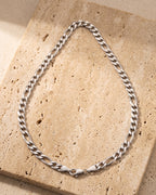 The whole silver Atlas polished figaro chain lying on warm travertine stone