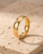 The whole gold-tone Atlas polished gold-tone band ring lying on warm travertine stone