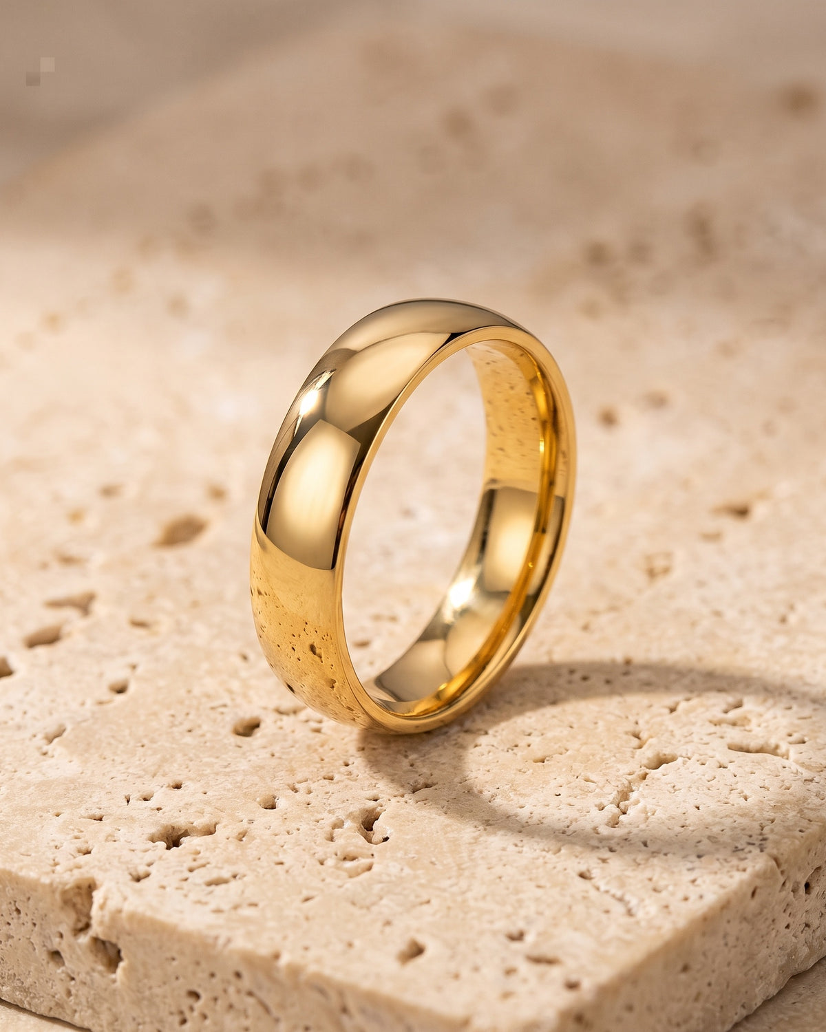 The whole gold-tone Atlas polished gold-tone band ring lying on warm travertine stone