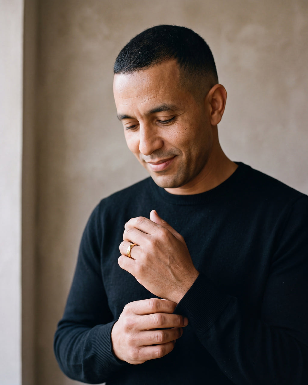 Man in a black merino crew-neck sweater by a window wearing the gold-tone Atlas polished gold-tone band ring