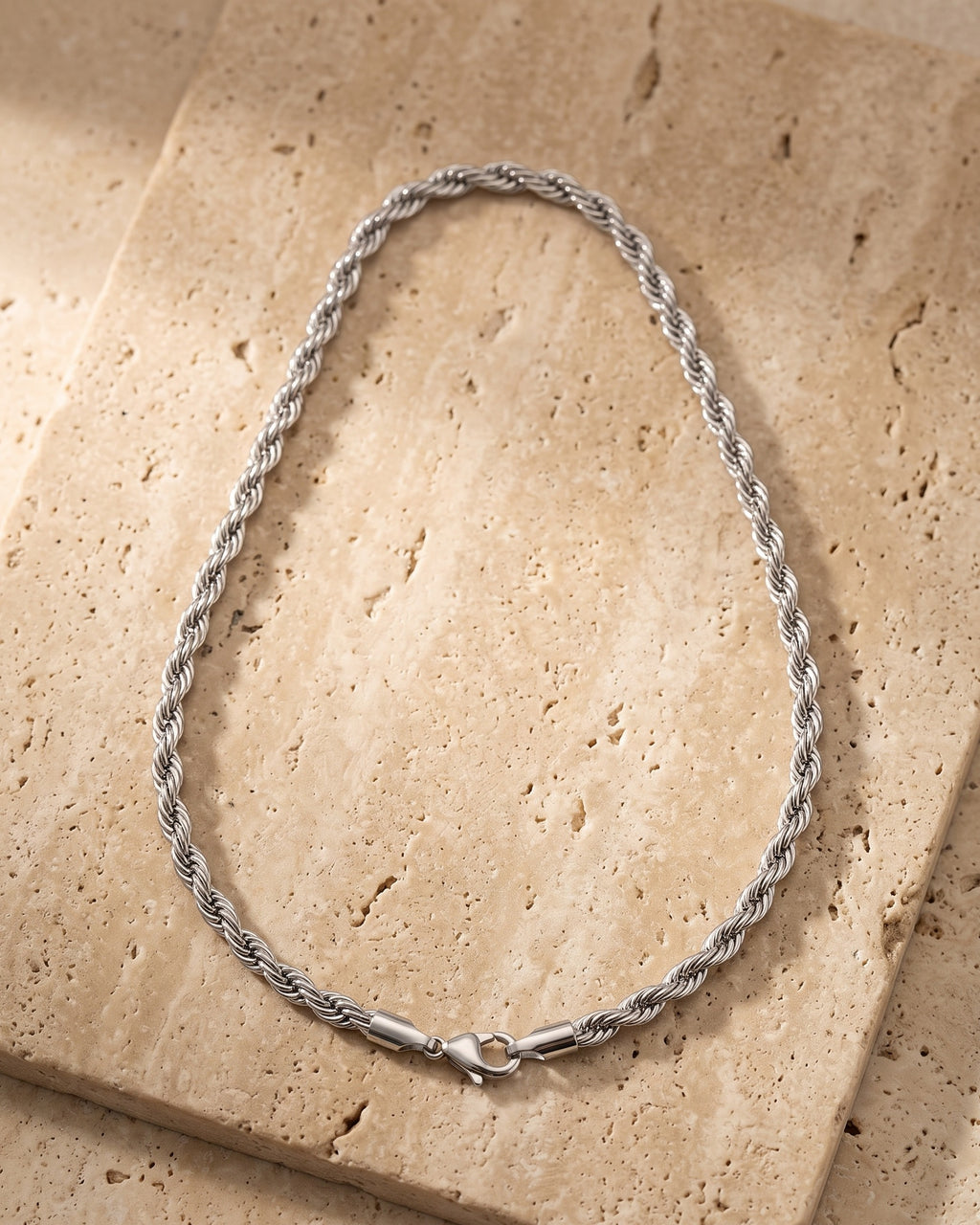 The whole silver-tone Atlas Polished Rope Chain lying on warm travertine stone