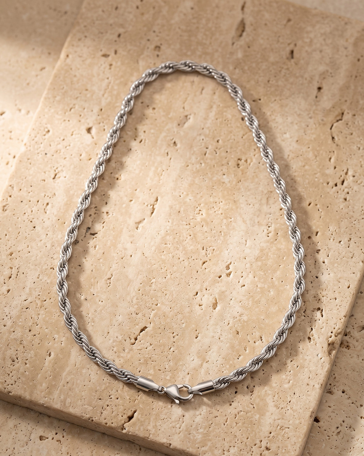The whole silver-tone Atlas Polished Rope Chain lying on warm travertine stone
