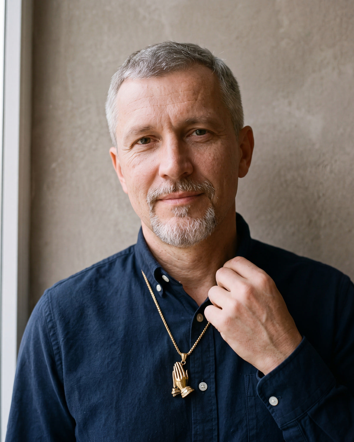Man in a navy shirt wearing the gold-tone Atlas praying hands pendant necklace