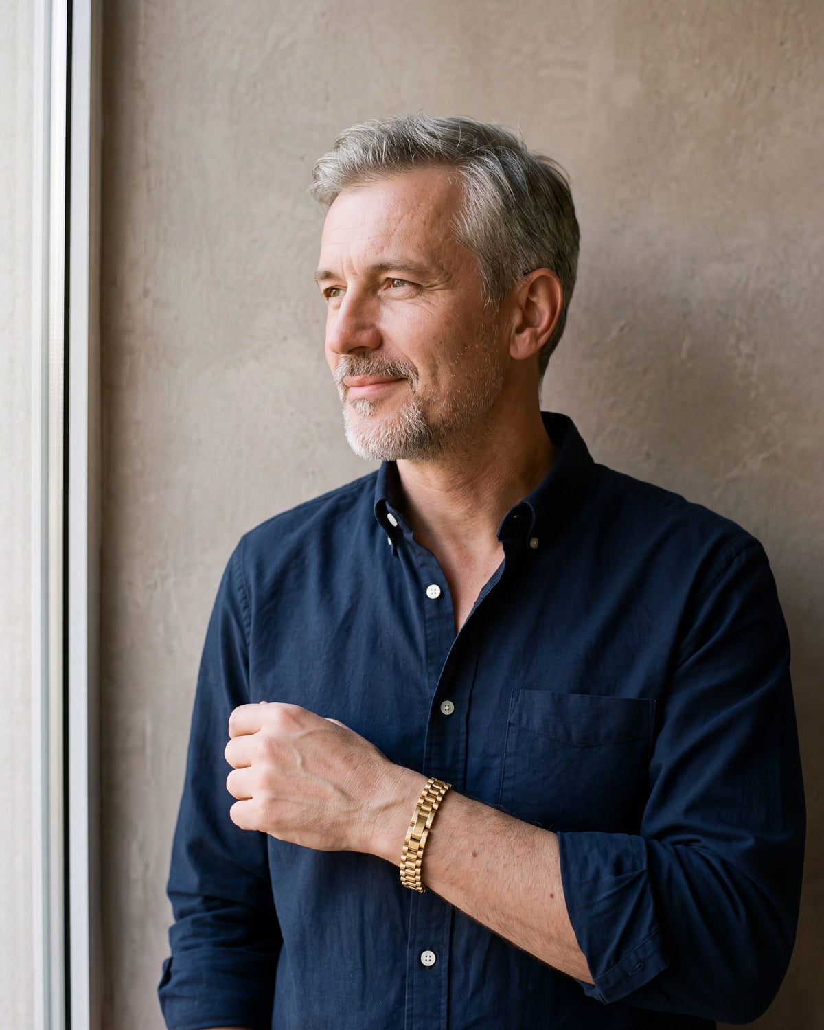 Man in a navy shirt by a window wearing the gold-tone Atlas President link bracelet