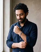Man in a navy shirt by a window adjusting his cuff, wearing the silver Atlas President link bracelet