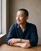 Man in a navy linen shirt seated at a table, wearing the gold-tone Atlas President link bracelet