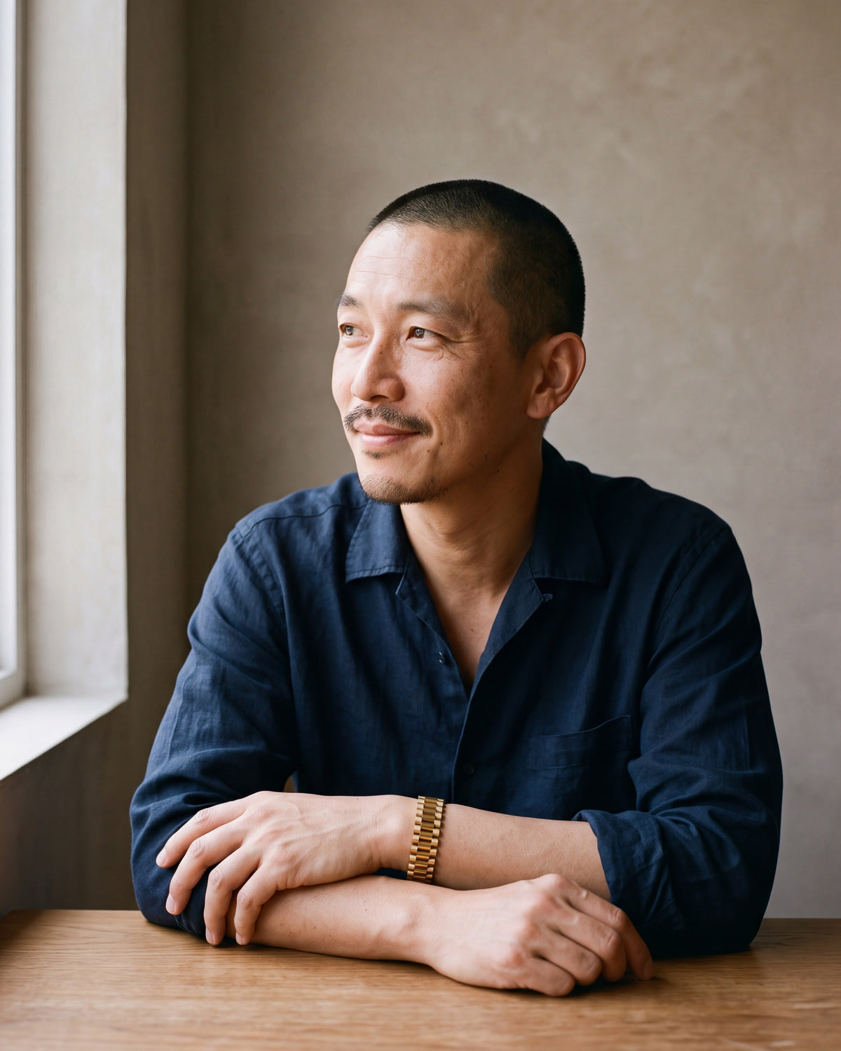 Man in a navy linen shirt seated at a table, wearing the gold-tone Atlas President link bracelet