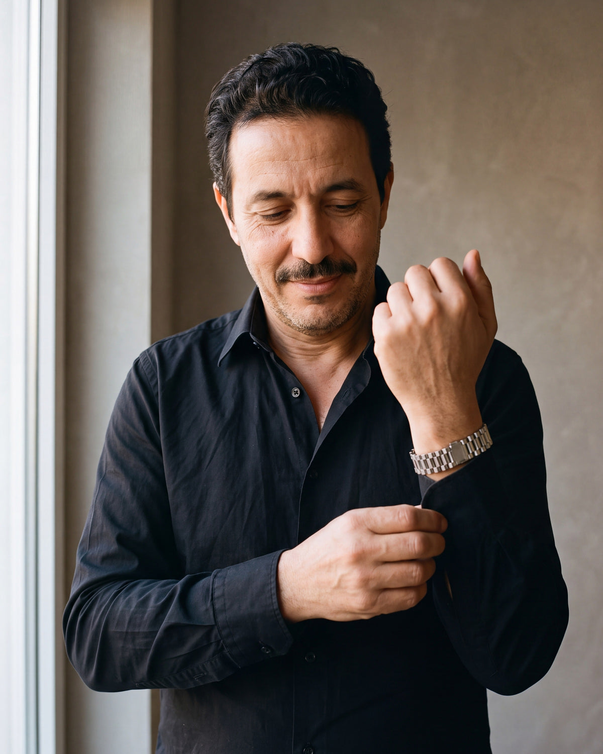 Man in a black shirt adjusting his cuff, wearing the silver-tone Atlas President link bracelet