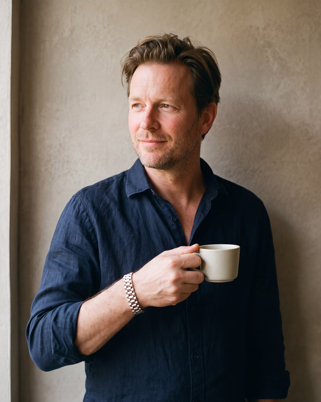 Man in a dark navy linen shirt by a window wearing the silver-tone Atlas president link bracelet