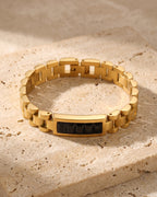 The whole gold-tone with black stones Atlas president link inlay bracelet lying on warm travertine stone