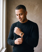 Man in a black merino crew-neck sweater by a window wearing the gold-tone with black stones Atlas president link inlay bracelet