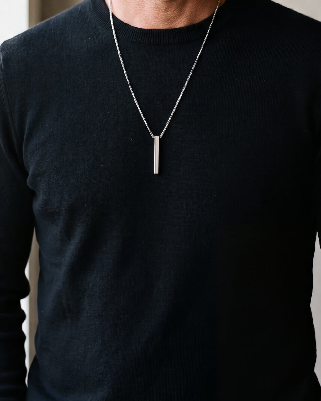Close-up of the 40 mm silver-tone Atlas bar pendant worn on a black sweater