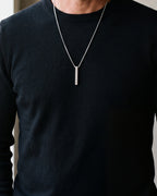 Close-up of the 40 mm silver-tone Atlas bar pendant worn on a black sweater