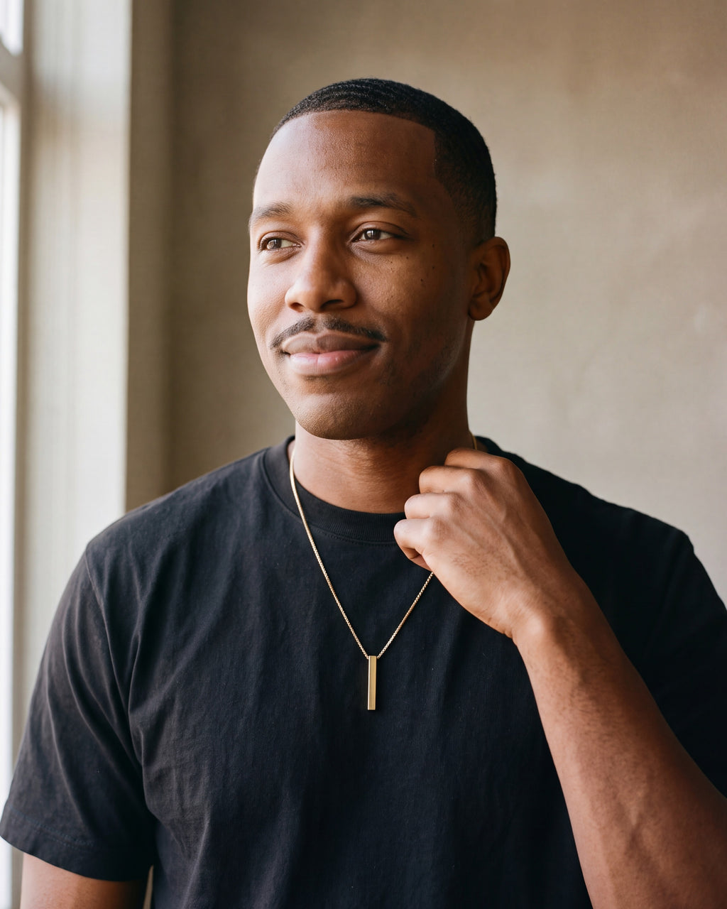 Man in a black T-shirt wearing the gold-tone Atlas bar pendant necklace