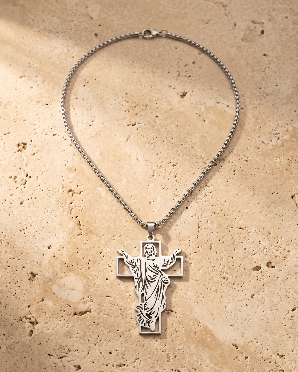 The whole silver-tone Atlas Risen Christ cross necklace laid on warm stone
