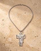 The whole silver-tone Atlas Risen Christ cross necklace laid on warm stone