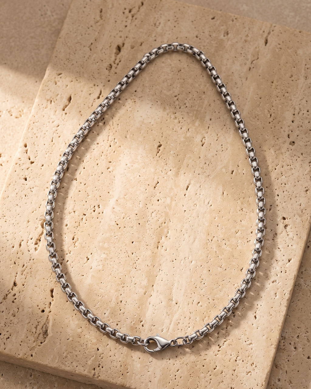 The whole silver-tone Atlas Rolo Chain lying on warm travertine stone