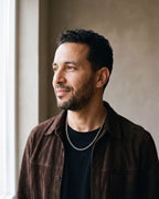 Man in a dark brown suede overshirt open over a black t-shirt by a window wearing the silver-tone Atlas Rolo Chain