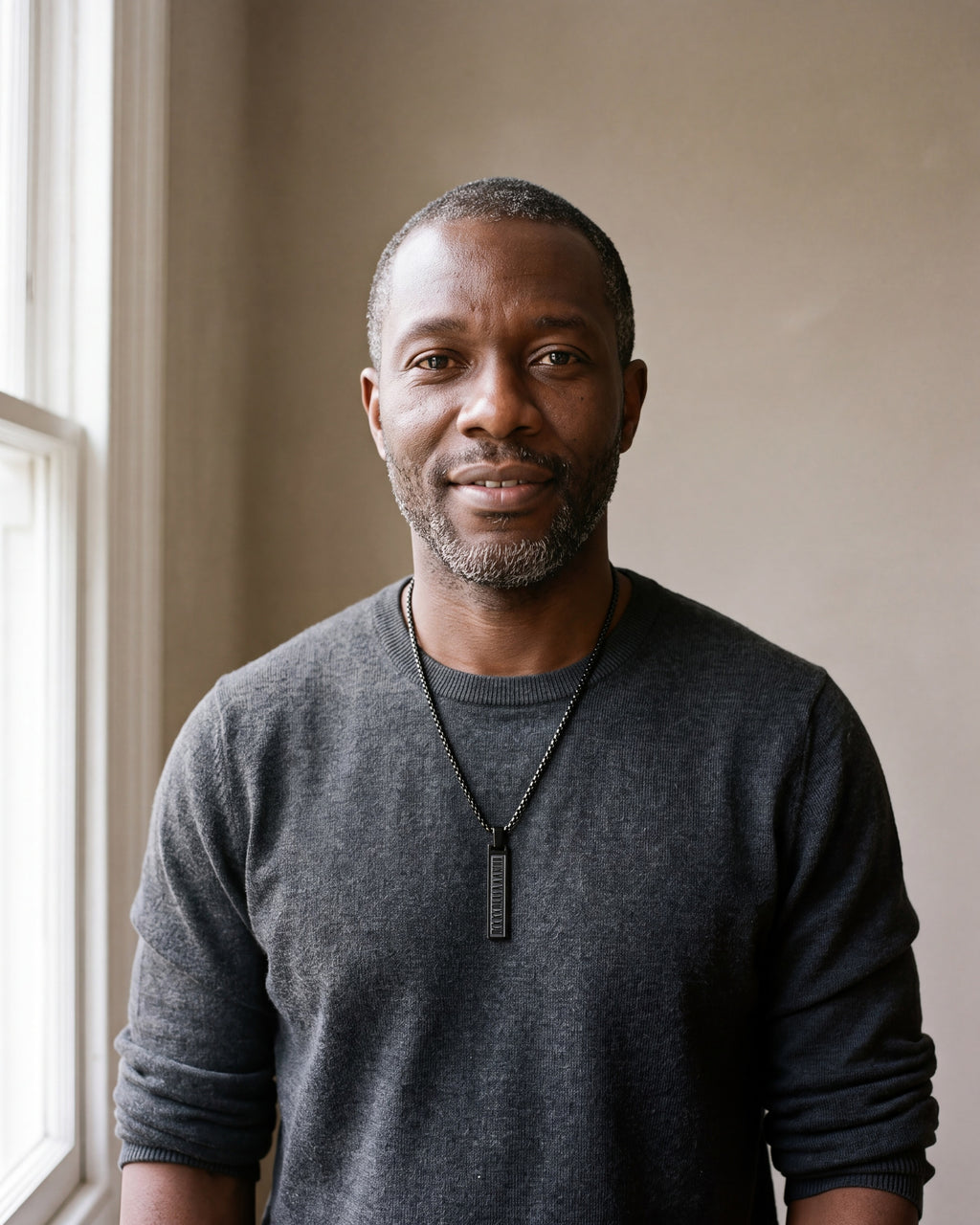 Man in a charcoal sweater wearing the black Atlas Roman numeral bar necklace