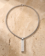 The whole silver-tone Atlas Roman numeral bar necklace laid on warm stone