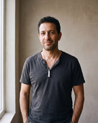 Man in a charcoal henley with his hands in his pockets wearing the silver-tone Atlas Roman numeral bar necklace