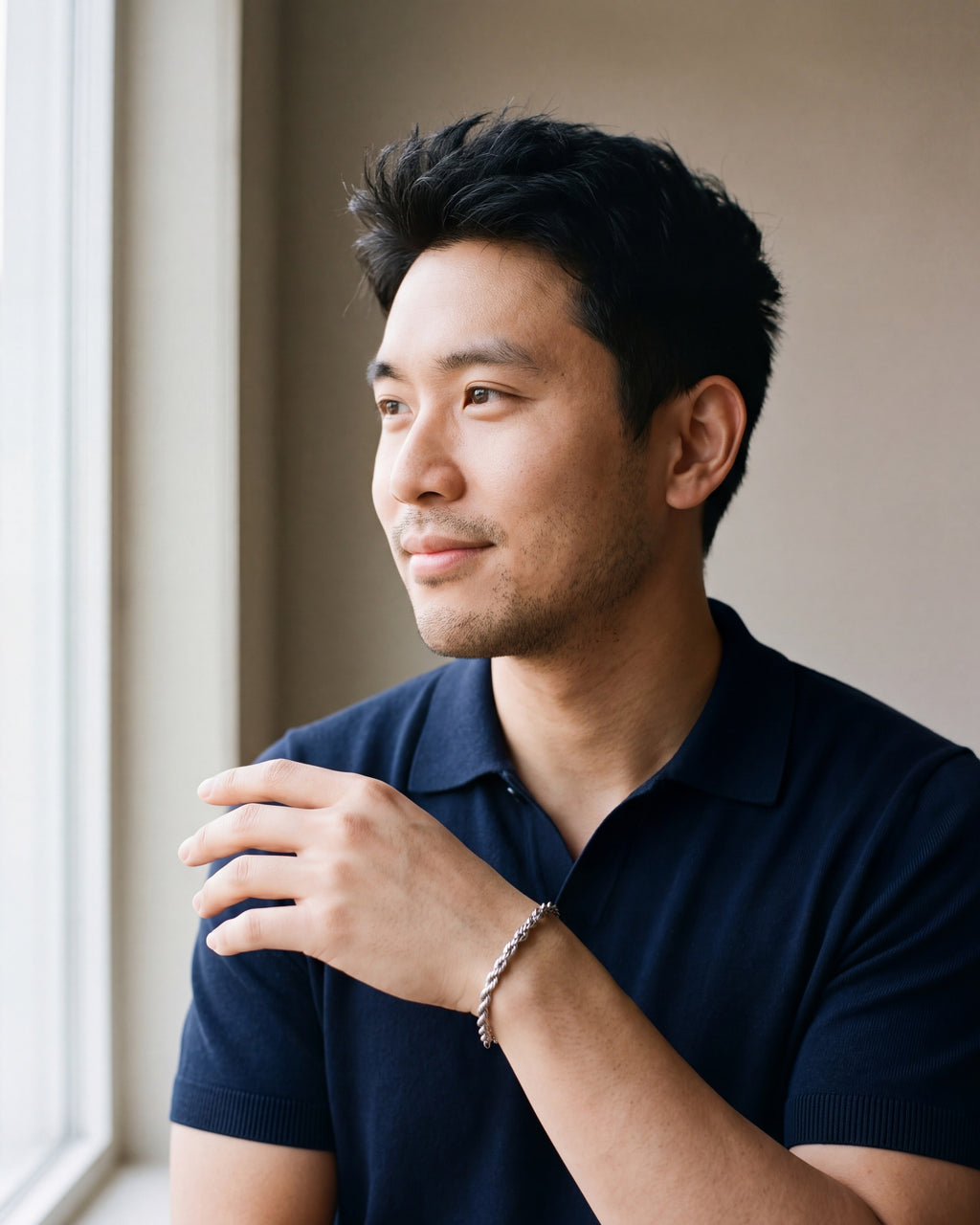 Man in a navy fine-gauge knit polo with an open collar by a window wearing the silver Atlas rope chain bracelet