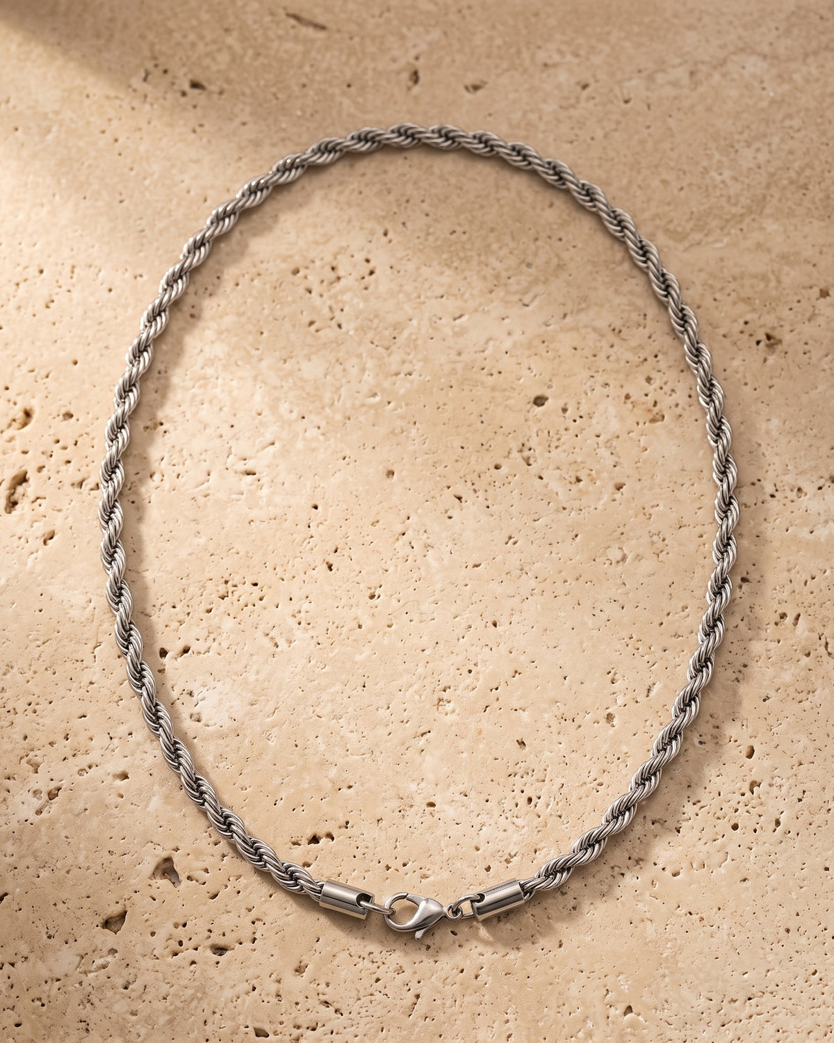 The whole silver-tone Atlas Rope Chain lying on warm travertine stone