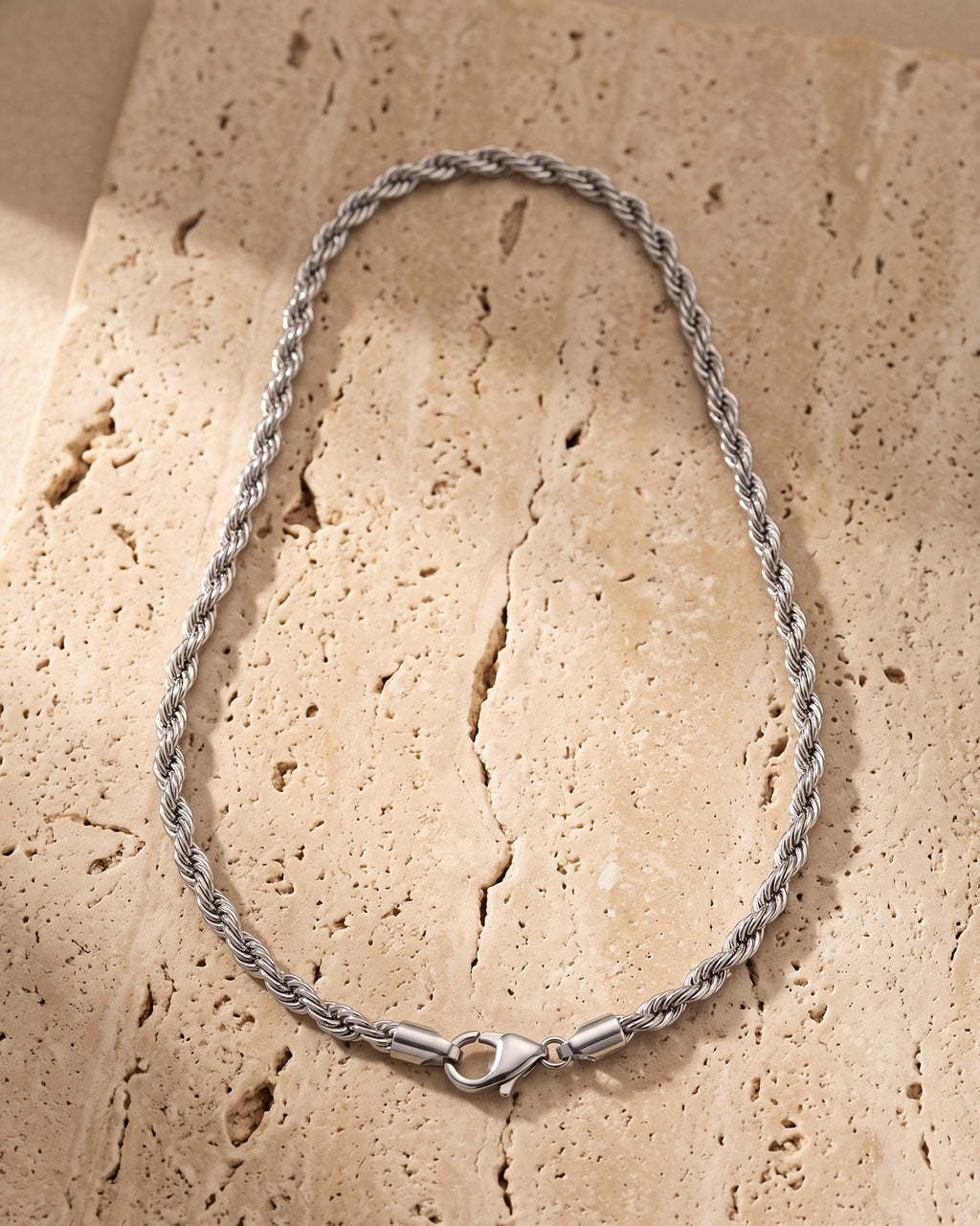 Atlas silver rope chain laid whole on warm stone, lobster clasp closed