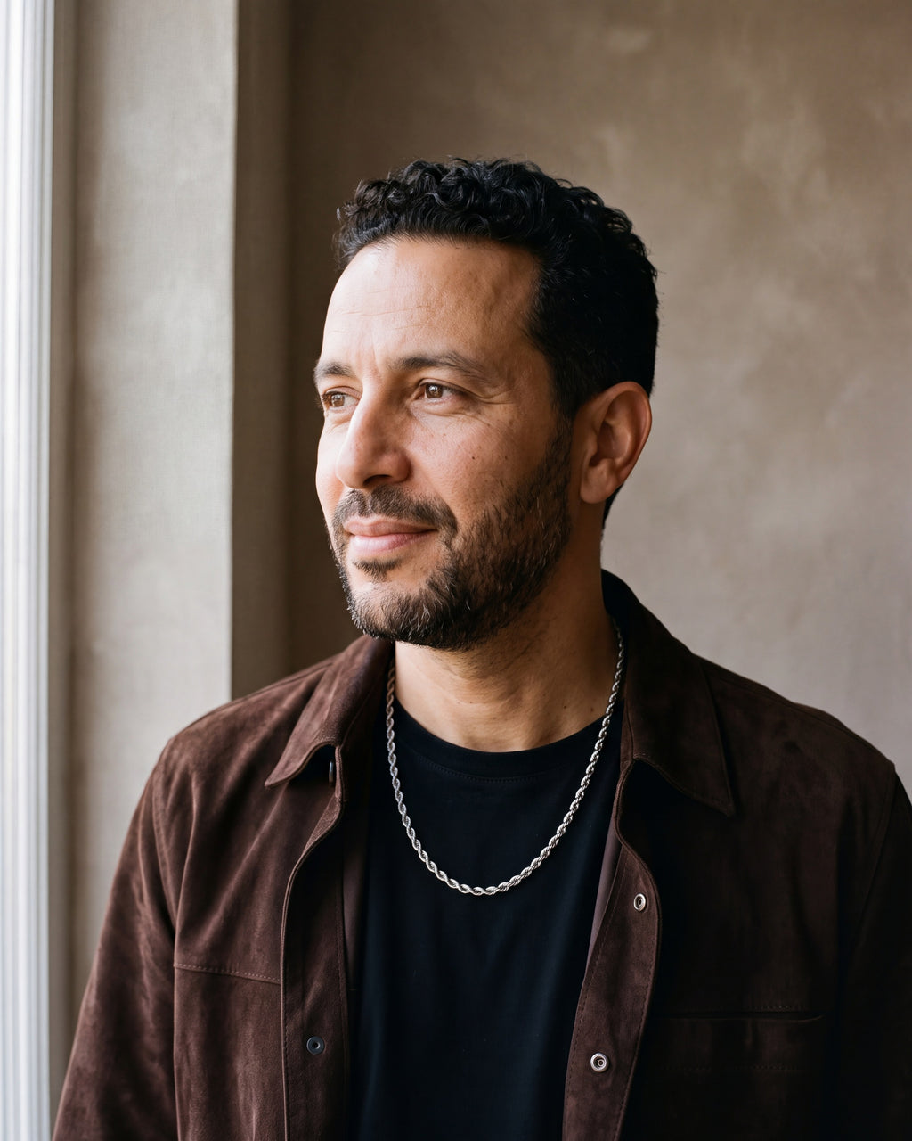 Man in a dark brown suede overshirt open over a black t-shirt by a window wearing the silver-tone Atlas Rope Chain