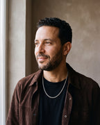 Man in a dark brown suede overshirt open over a black t-shirt by a window wearing the silver-tone Atlas Rope Chain