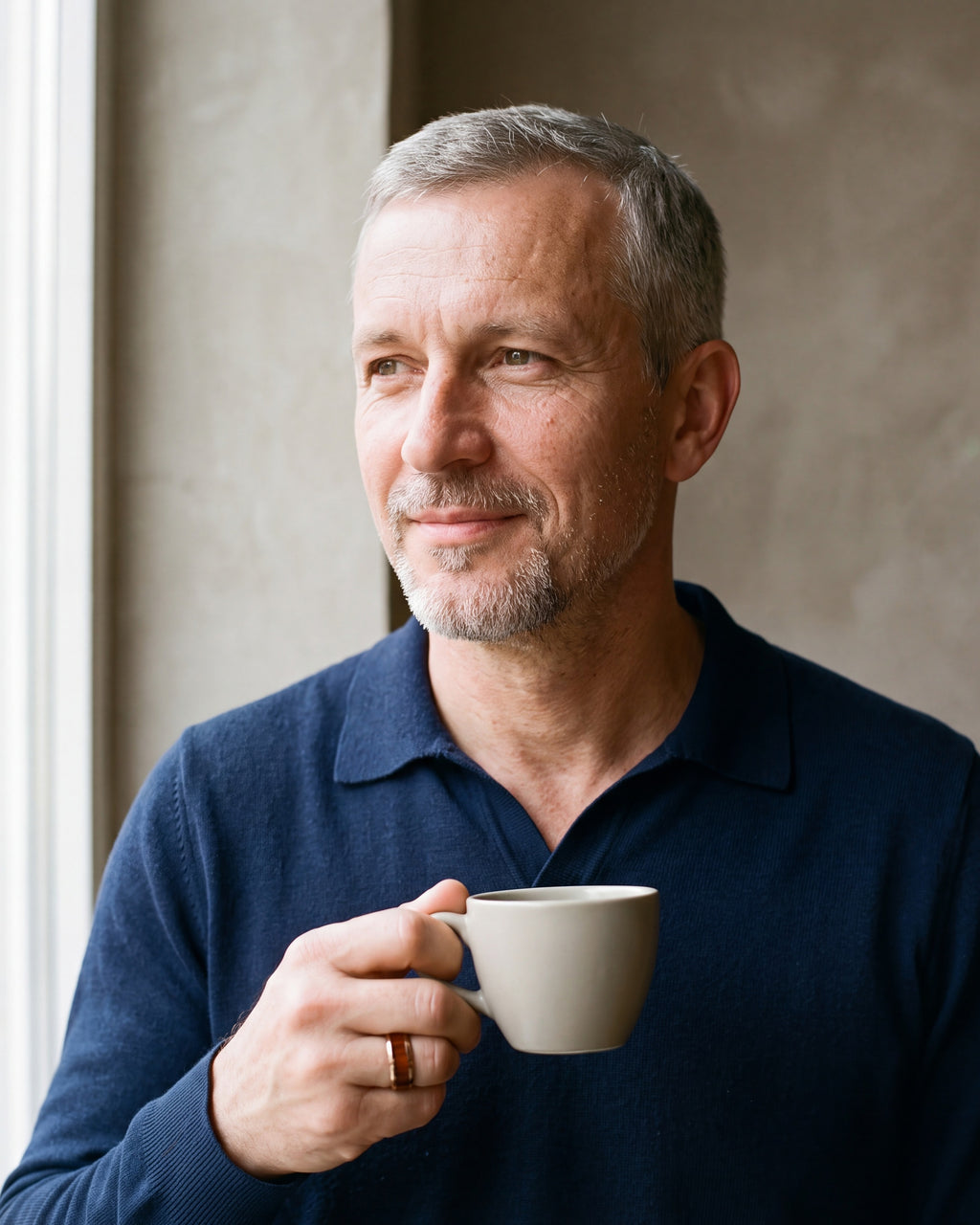Man in a navy knit polo holding a coffee cup, wearing the Atlas rose gold-tone wood inlay ring