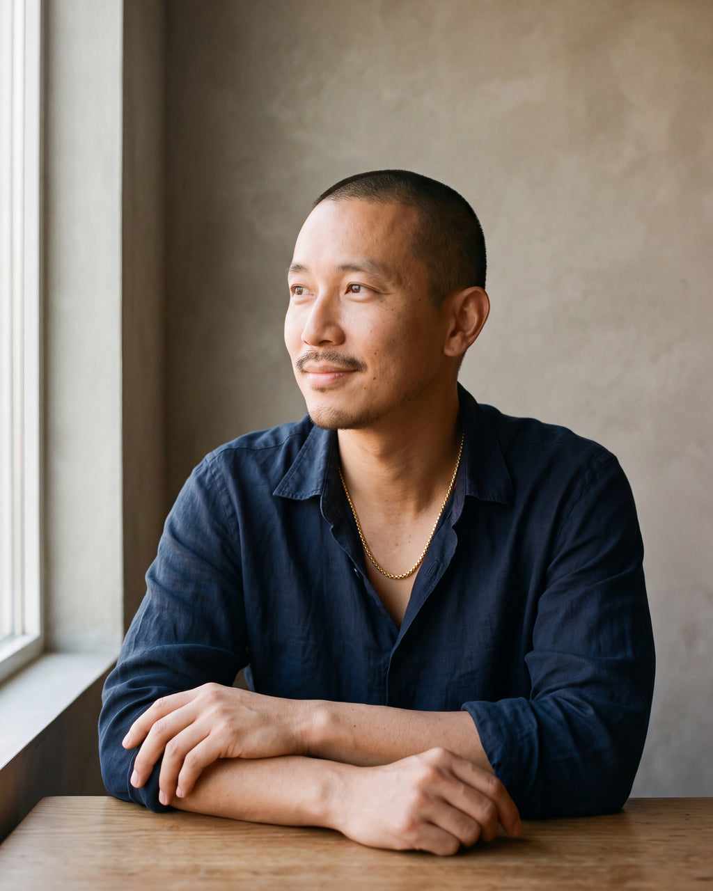 Man in a navy linen shirt seated by a window, wearing the 3 mm gold-tone Atlas round box chain