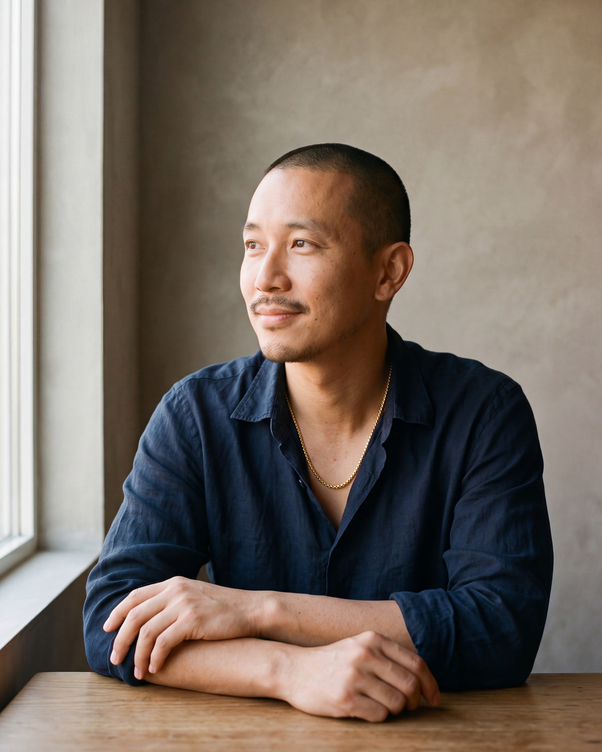 Man in a navy linen shirt seated by a window, wearing the 3 mm gold-tone Atlas round box chain