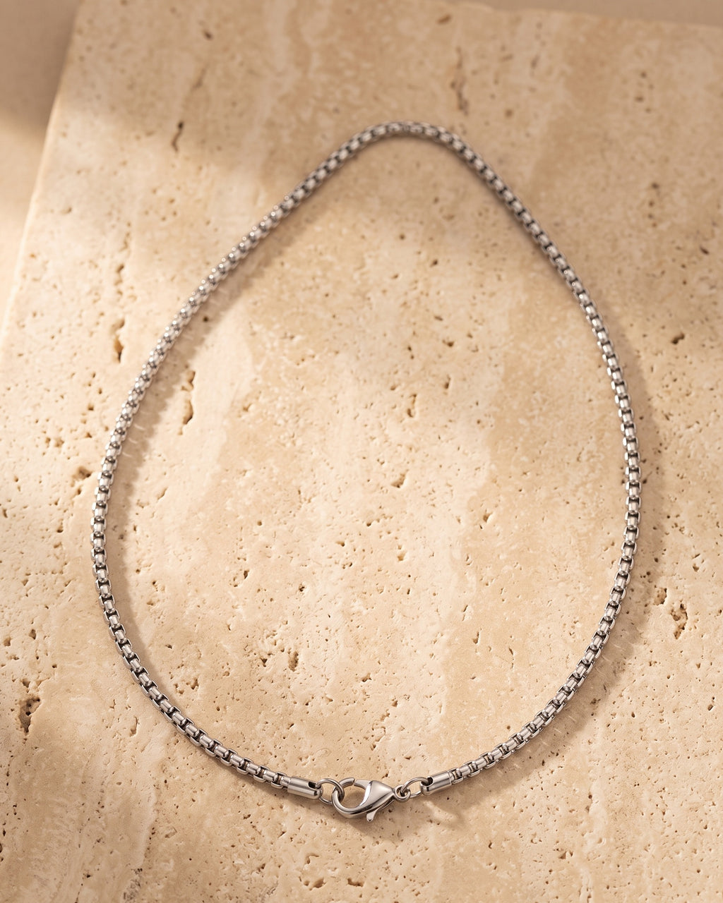 The whole silver Atlas round box chain laid on warm stone, lobster clasp closed