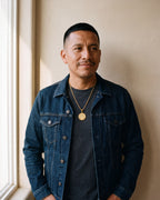 Second man in a dark indigo denim jacket open over a charcoal crew-neck t-shirt wearing the gold-tone Atlas saint benedict medal necklace