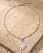 The whole silver-tone Atlas two-sided Saint Benedict medal necklace laid on warm stone