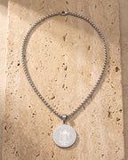 The whole silver-tone Atlas saint benedict medal necklace laid on warm stone