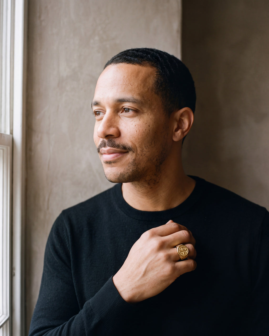 Man in a black merino sweater by a window wearing the gold-tone Atlas Saint Benedict signet ring