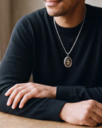 Close-up of the silver-tone Atlas Saint Christopher oval pendant necklace worn by a man, shown at true size