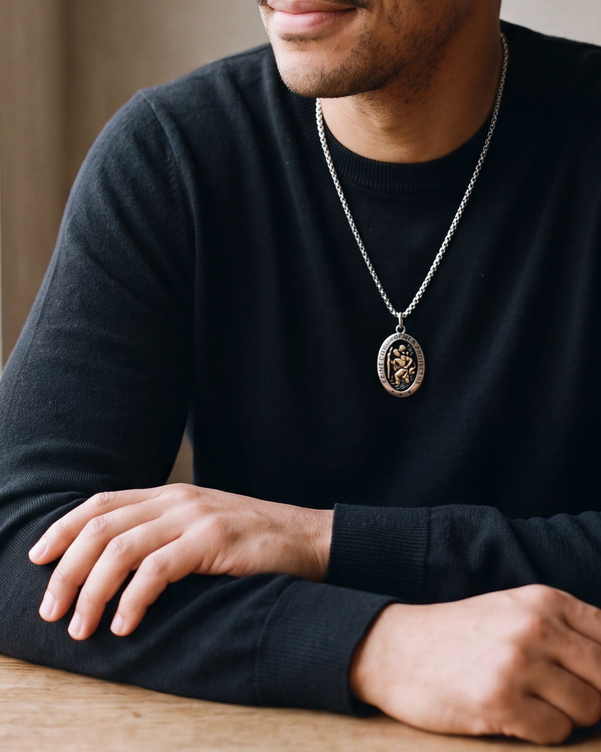 Close-up of the silver-tone Atlas Saint Christopher oval pendant necklace worn by a man, shown at true size