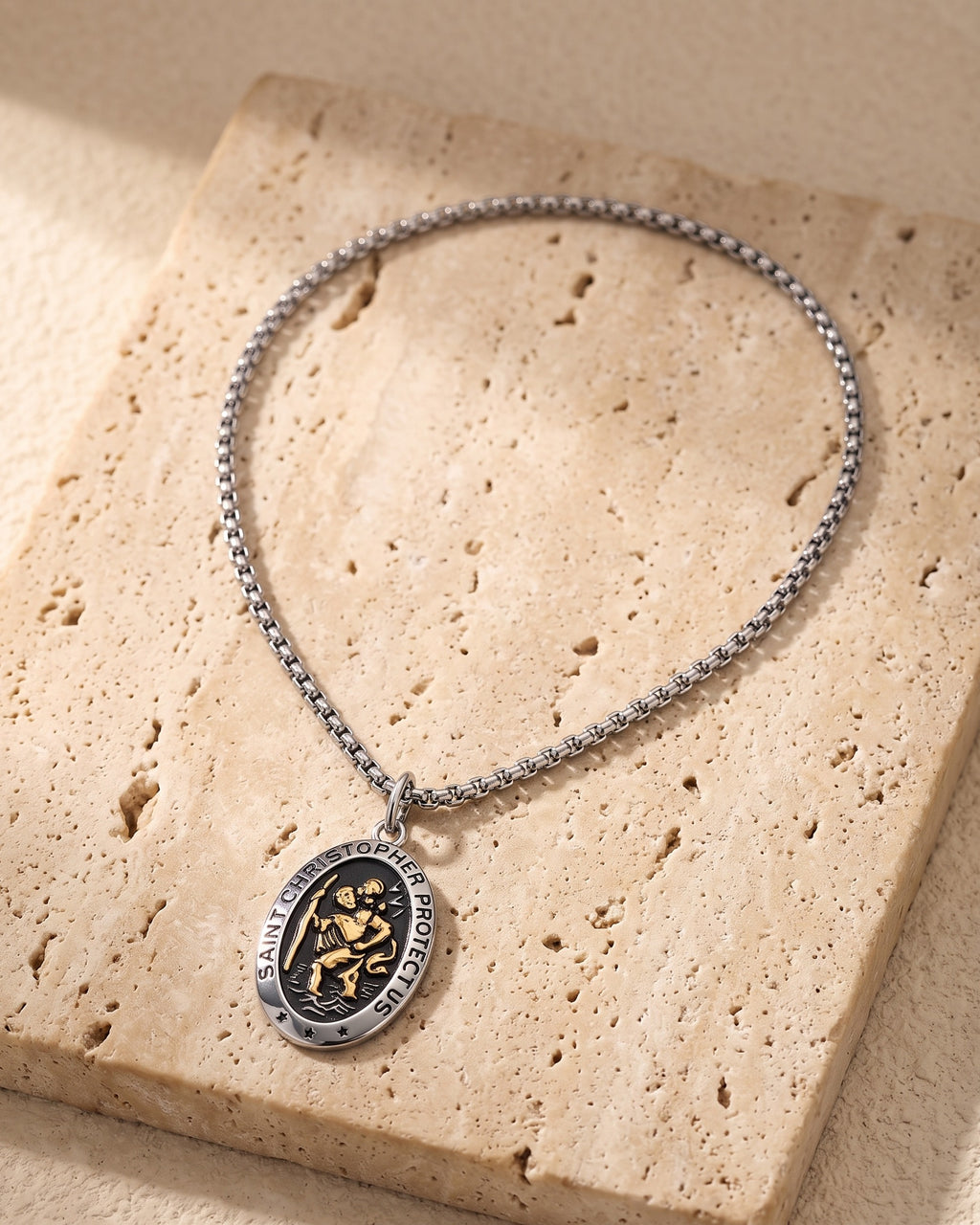The whole silver-tone Atlas Saint Christopher oval pendant necklace laid on warm stone
