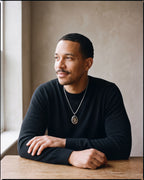 Man in a black merino sweater seated at a wooden table wearing the silver-tone Atlas Saint Christopher oval pendant necklace