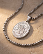 Close-up of the silver-tone Atlas Saint Michael oval medal on warm stone