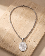 The whole silver-tone Atlas Saint Michael oval pendant necklace laid on warm stone