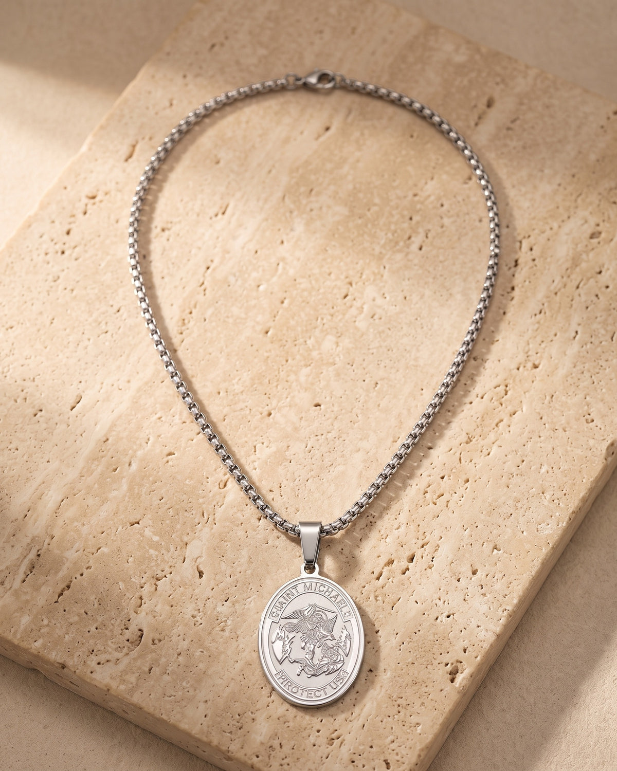 The whole silver-tone Atlas Saint Michael oval pendant necklace laid on warm stone