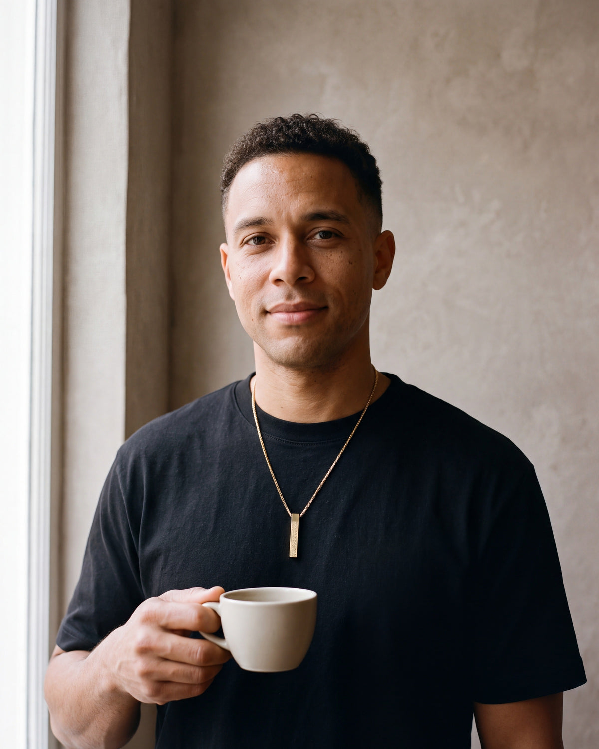 Second man in a plain heavyweight black cotton crew-neck t-shirt (thick wearing the gold-tone Atlas script bar pendant necklace