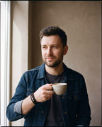 Man in a denim jacket holding a coffee cup wearing the black Atlas scrollwork bead braided leather bracelet