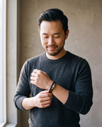 Man in a charcoal sweater adjusting his sleeve wearing the black Atlas scrollwork bead braided leather bracelet