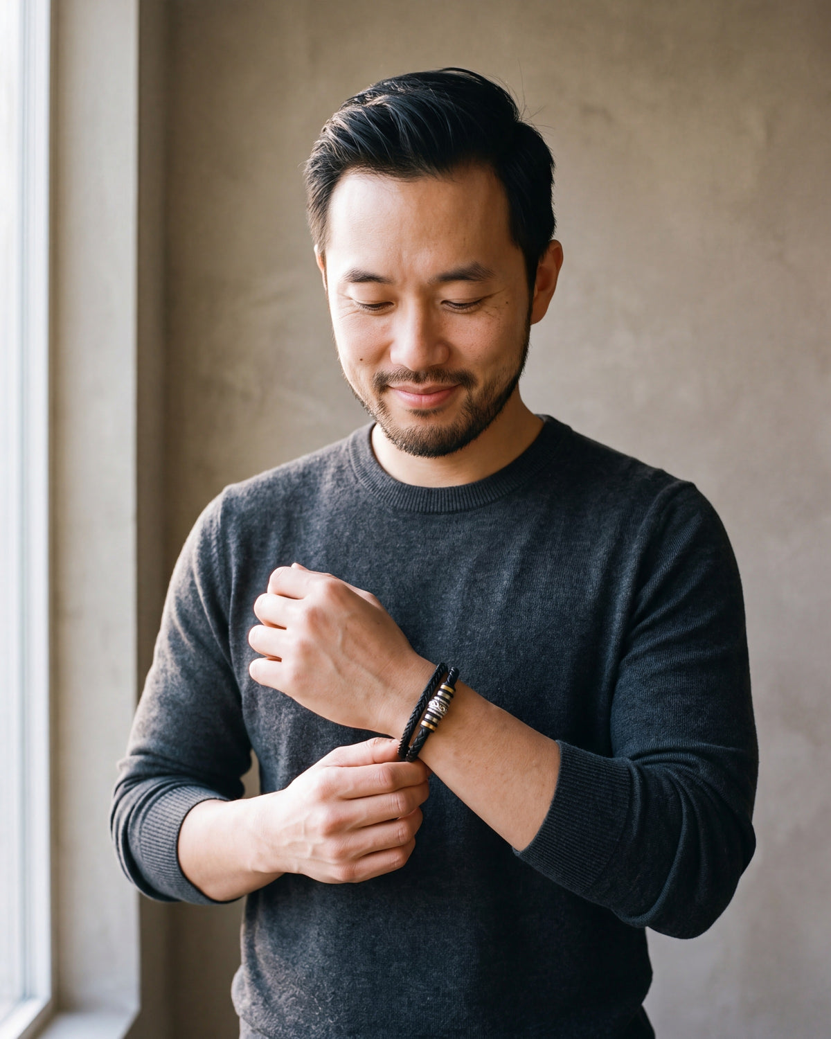 Man in a charcoal sweater adjusting his sleeve wearing the black Atlas scrollwork bead braided leather bracelet