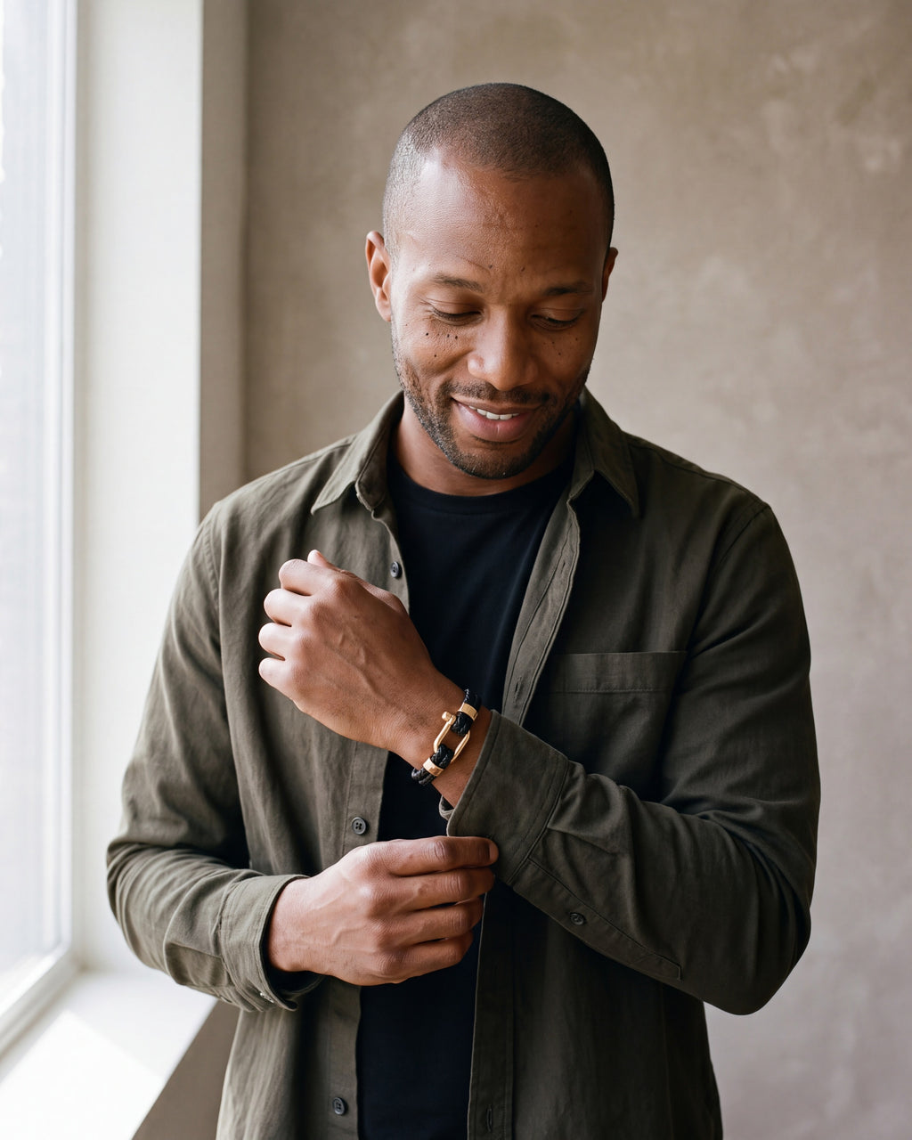 Man in a dark olive overshirt open over a black t-shirt wearing the gold-tone / black Atlas Shackle Bracelet in Braided Leather